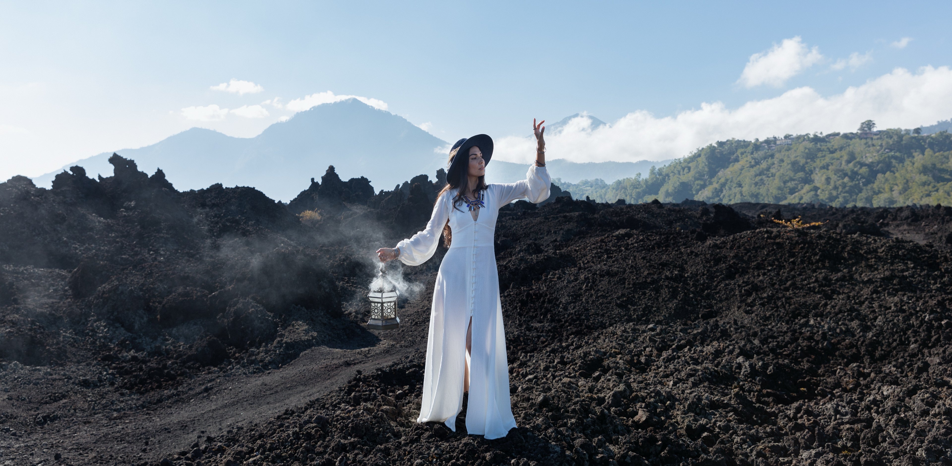 Woman in a white Kayame dress walking across the black lava fields of Mount Batur, Bali